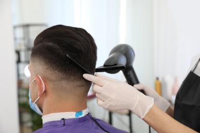 Photo of Professional stylist working with client in salon, closeup. Hairdressing services during Coronavirus quarantine