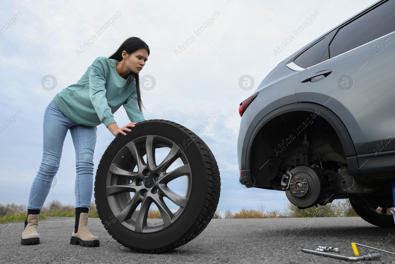 Photo of Young woman changing tire of car on roadside