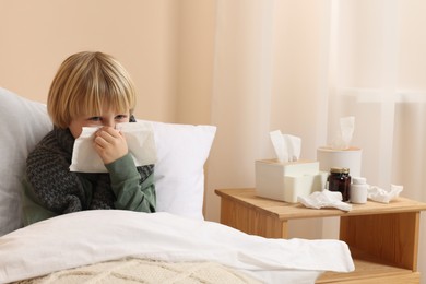 Photo of Boy blowing nose in tissue in bed at home. Cold symptoms