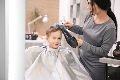 Photo of Professional female hairdresser working with little boy in salon