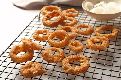 Photo of Cooling rack with homemade crunchy fried onion rings on light background