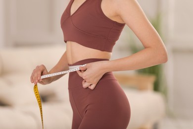 Woman in sportswear measuring waist with tape at home, closeup