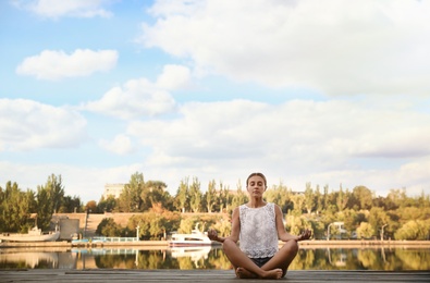 Photo of Young woman meditating near river at sunset, space for text. Nature healing power