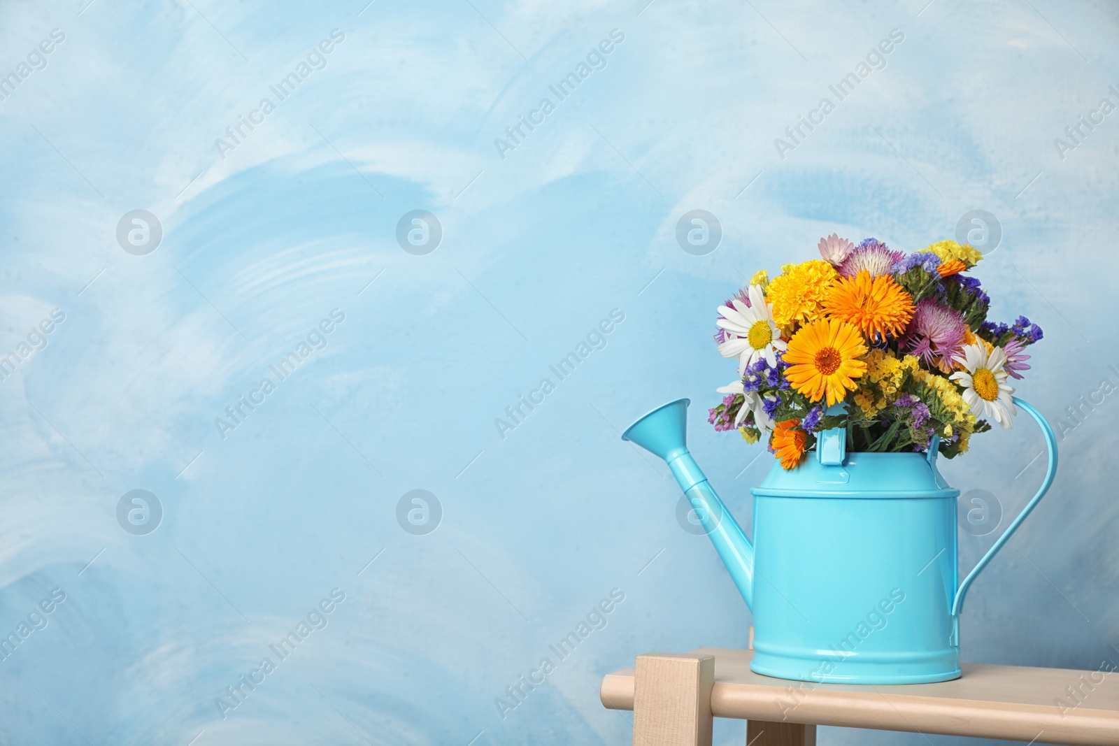 Photo of Watering can with beautiful wild flowers on table against color background