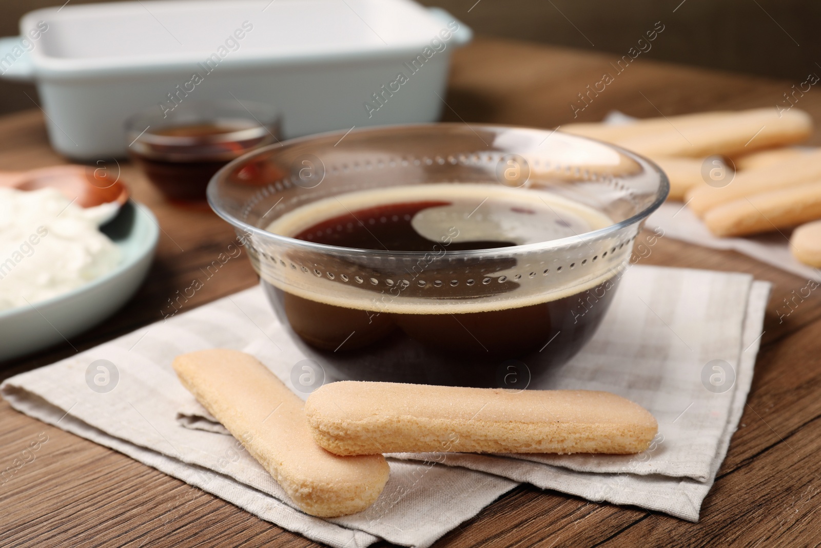 Photo of Bowl of coffee and savoiardi biscuit cookies on wooden table. Making tiramisu cake