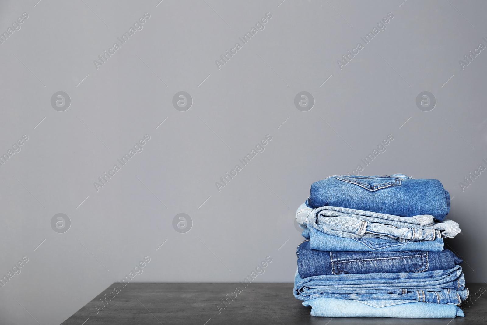 Photo of Stack of different jeans on  table against gray background. Space for text