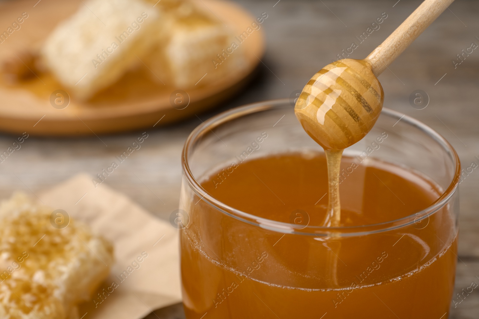 Photo of Sweet honey dripping from dipper into glass jar, closeup