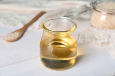 Photo of Jar of organic sesame oil on white wooden table, closeup