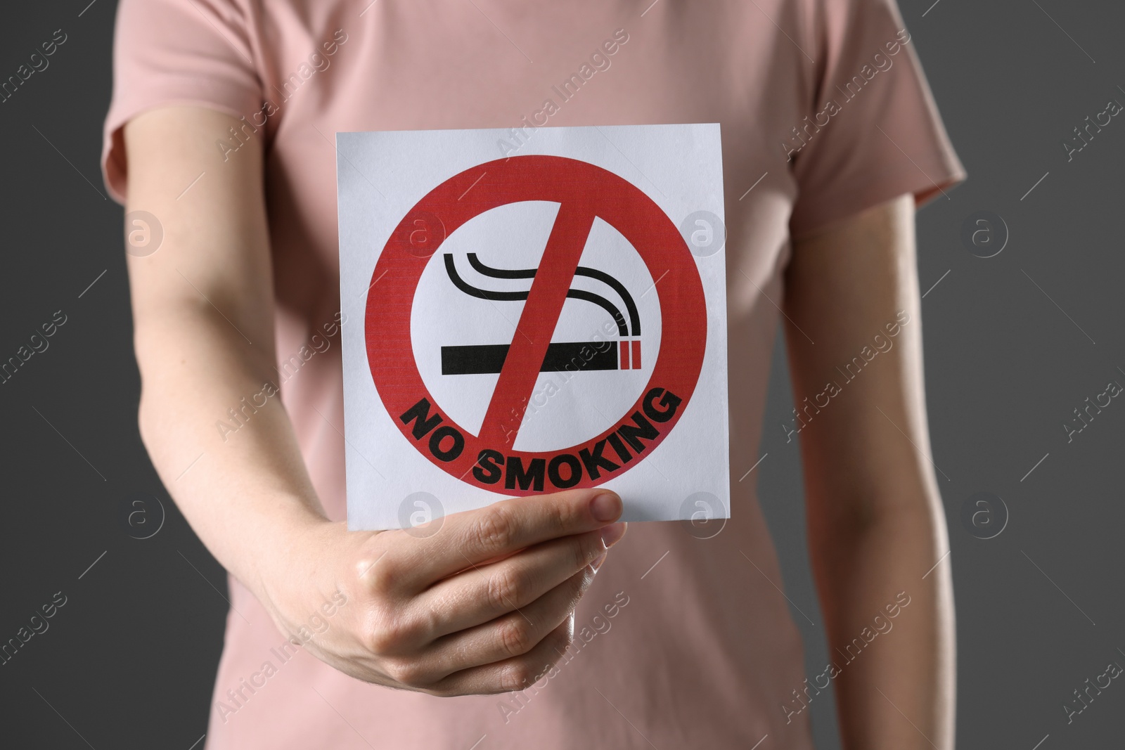 Photo of Woman holding card with no smoking sign on gray background, closeup