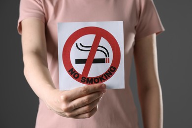 Woman holding card with no smoking sign on gray background, closeup