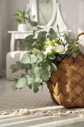 Stylish wicker basket with bouquet on floor in room