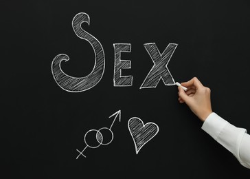 Image of Sexual education. Woman writing word Sex on blackboard, closeup. Chalked heart, female and male gender signs