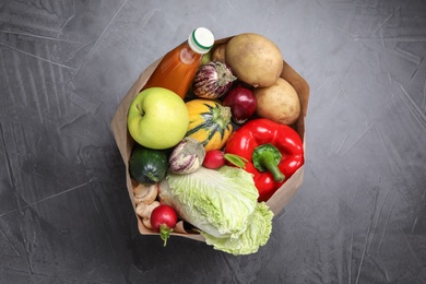 Photo of Paper package with fresh vegetables, apple and bottle of juice on dark background, top view
