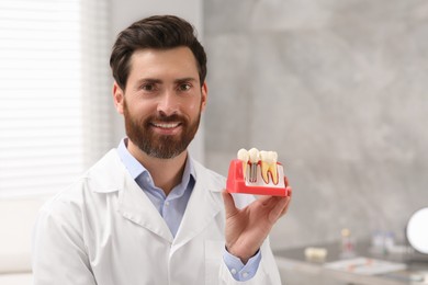 Doctor demonstrating educational model of dental implant in clinic, space for text