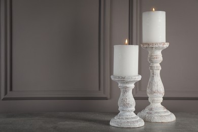 Photo of Elegant candlesticks with burning candles on grey table. Space for text