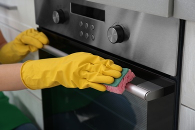 Photo of Woman cleaning kitchen oven with sponge, closeup