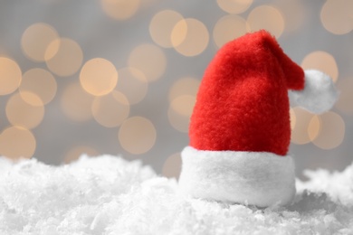 Mini Santa hat on artificial snow against blurred Christmas lights. Space for text