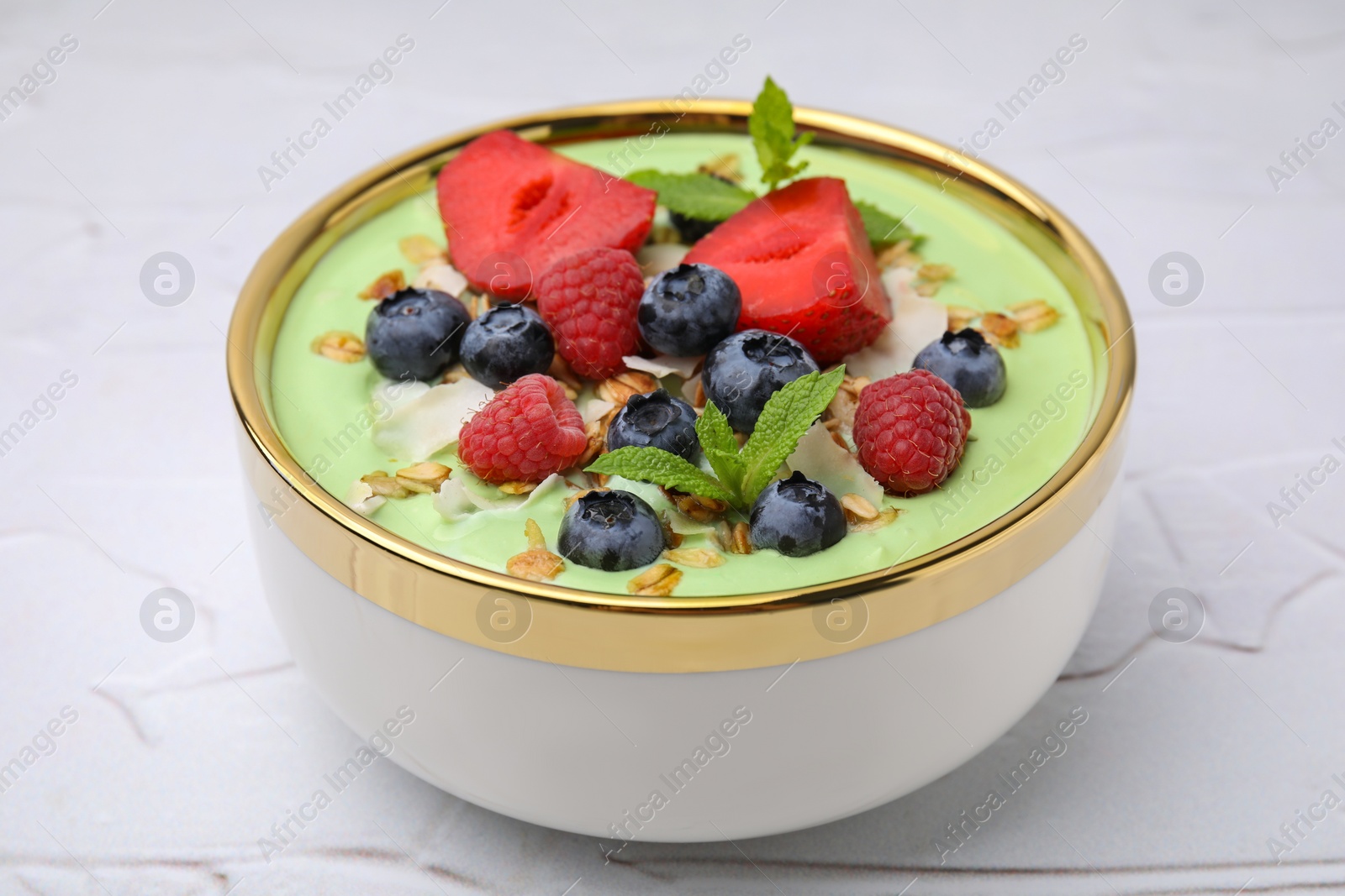 Photo of Tasty matcha smoothie bowl served with berries and oatmeal on white textured table, closeup. Healthy breakfast