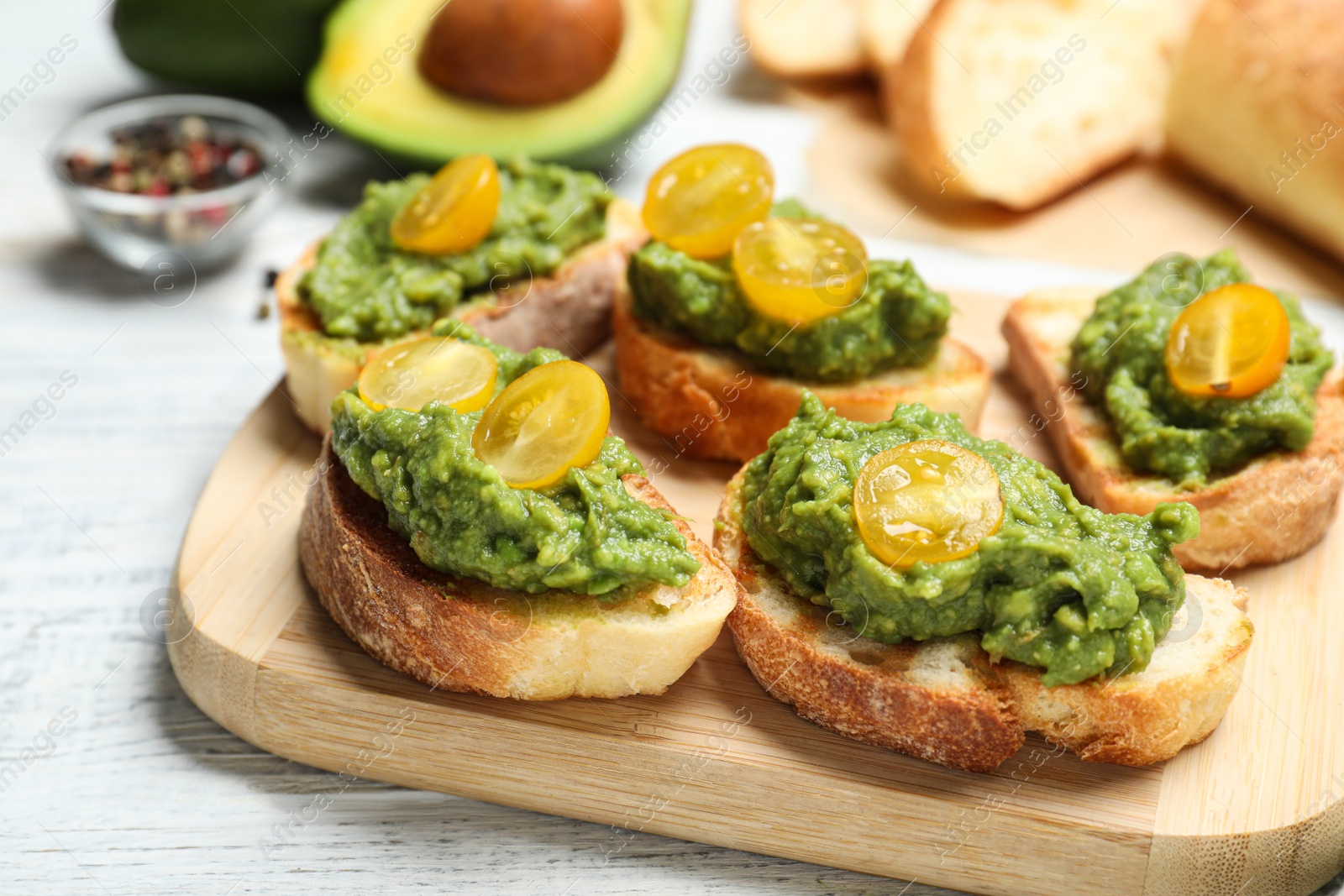 Photo of Tasty bruschettas with avocado and yellow cherry tomatoes on white wooden table, closeup