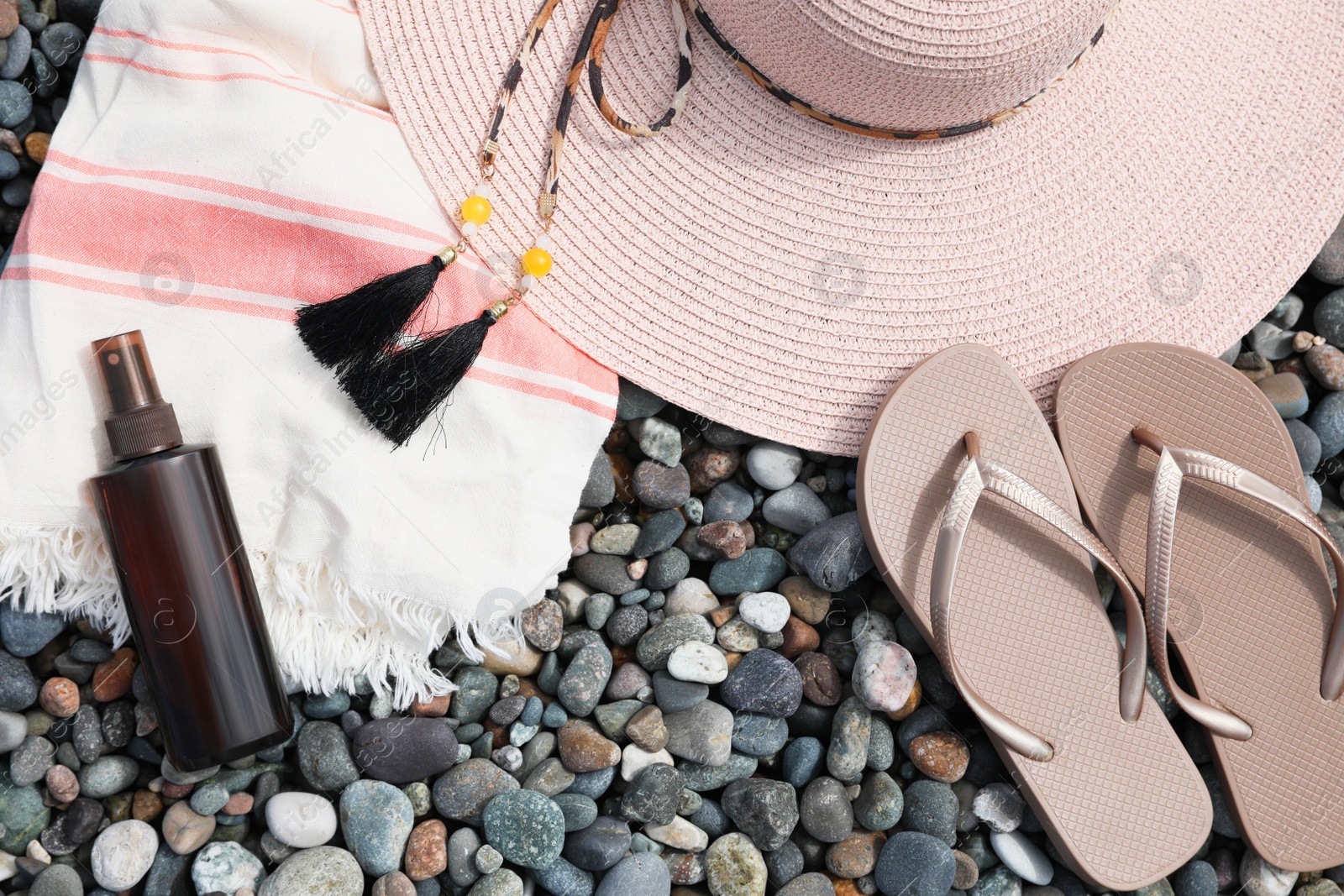 Photo of Beautiful hat, sunscreen and flip flops on pebbles, flat lay