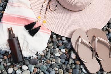 Photo of Beautiful hat, sunscreen and flip flops on pebbles, flat lay