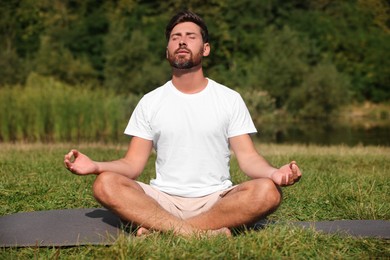 Man practicing yoga on mat outdoors. Lotus pose