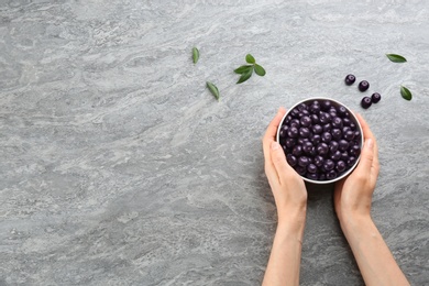 Woman holding bowl with tasty acai berries at light grey table, top view. Space for text