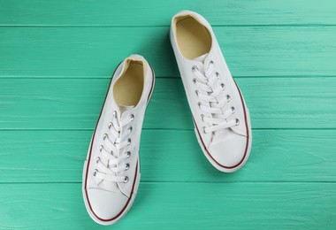 Photo of Pair of white sneakers on turquoise wooden table, flat lay