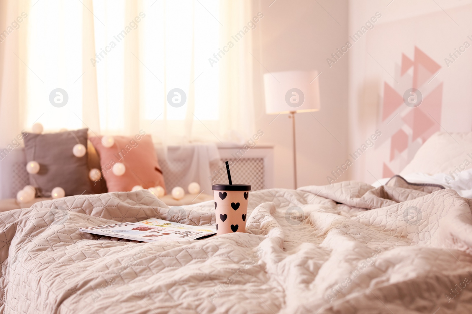 Photo of Cup of hot drink with magazines on bed at home