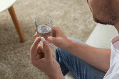 Photo of Man with glass of water and pill on blurred background, closeup