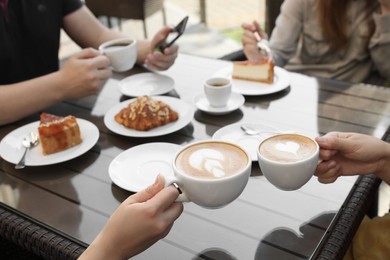 Photo of Friends drinking coffee at wooden table in outdoor cafe, closeup