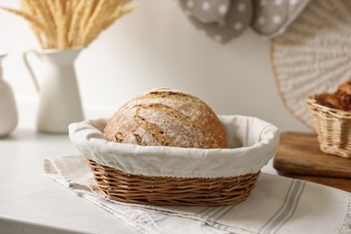 Photo of Wicker bread basket with freshly baked loaf on white marble table in kitchen