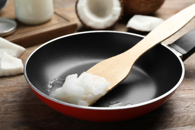 Frying pan with coconut oil and wooden spatula on wooden table. Healthy cooking