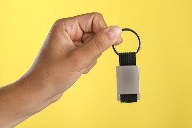 Woman holding metallic keychain on yellow background, closeup