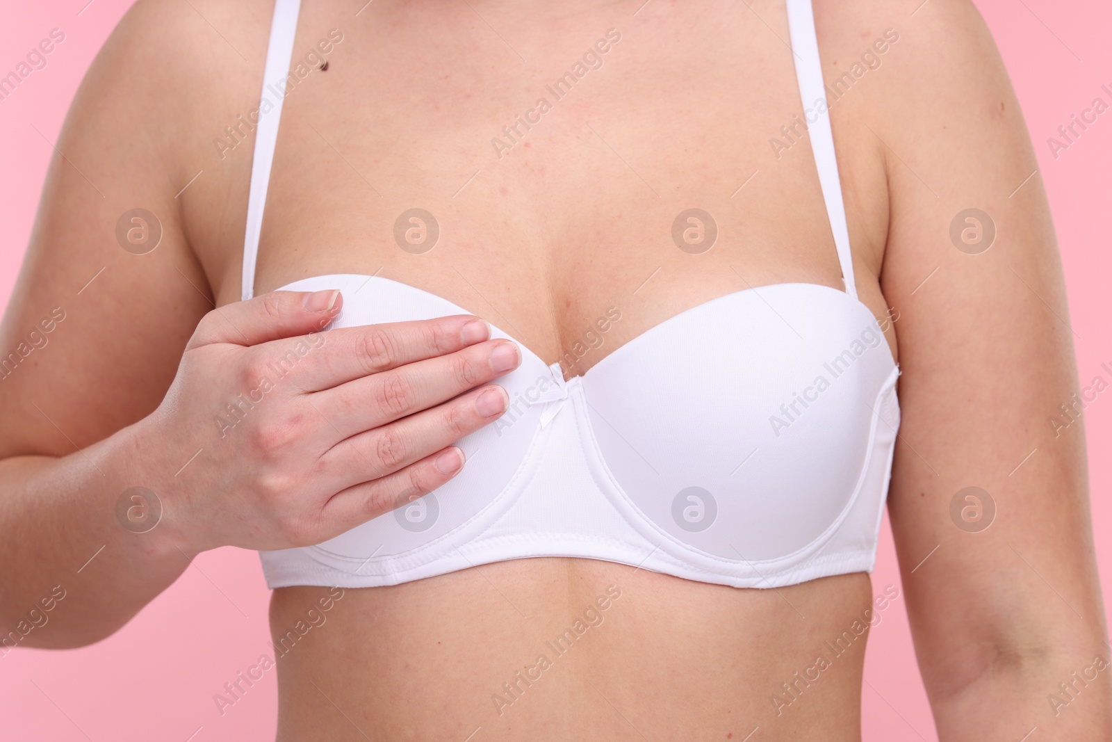 Photo of Mammology. Woman in bra doing breast self-examination on pink background, closeup