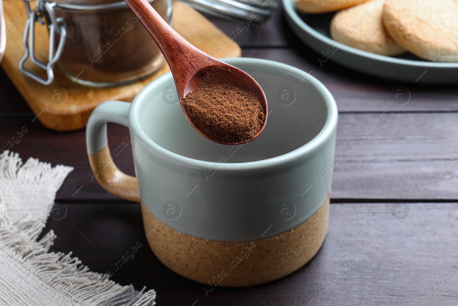 Photo of Spoon of instant coffee over mug on wooden table, closeup