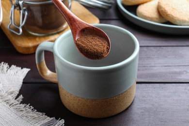 Photo of Spoon of instant coffee over mug on wooden table, closeup