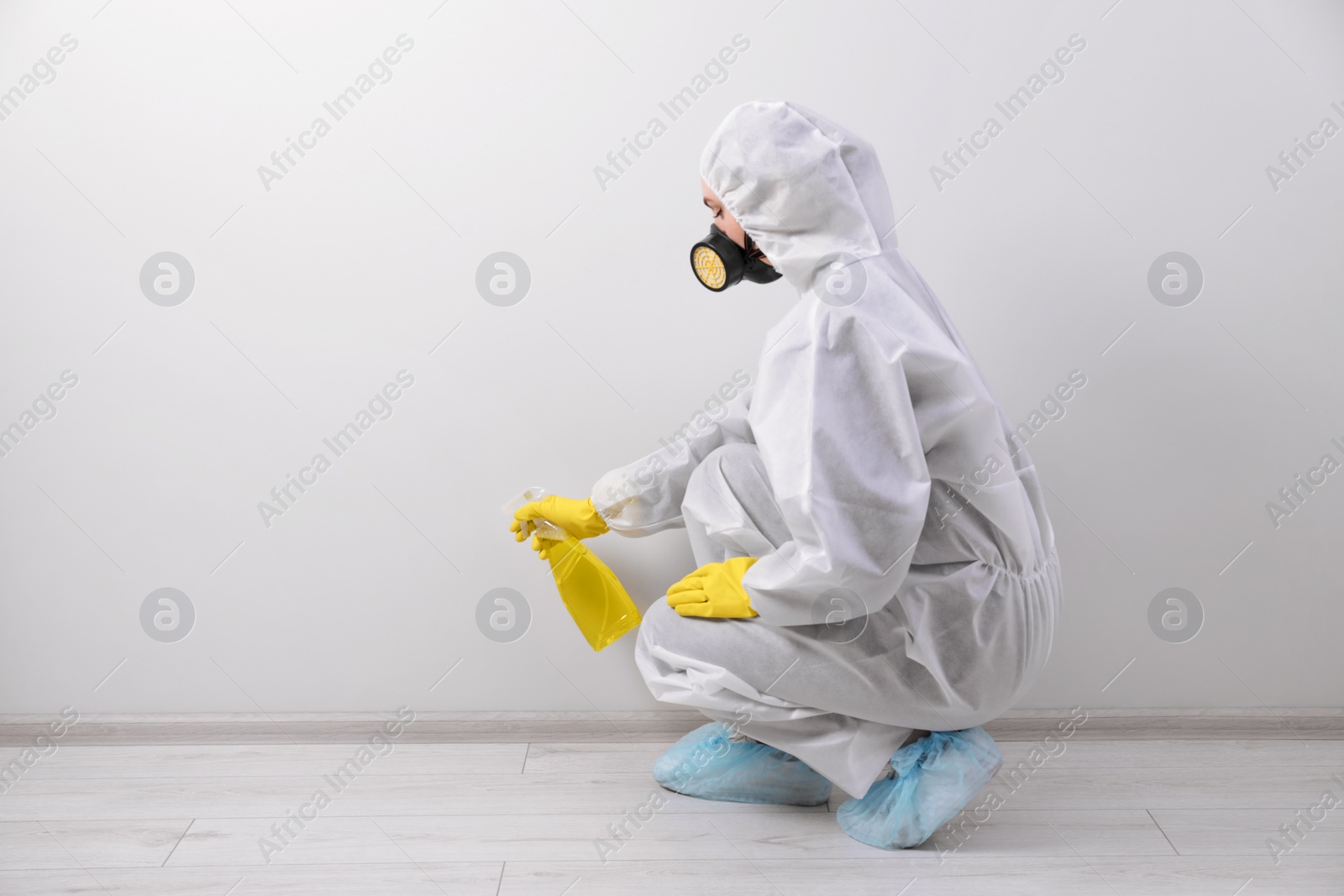 Photo of Woman in protective suit cleaning mold with sprayer on wall indoors