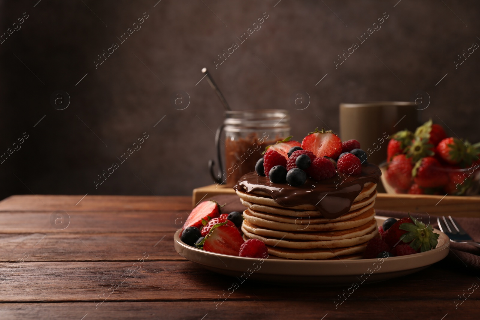 Photo of Stack of tasty pancakes with fresh berries and chocolate spread on wooden table, space for text