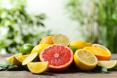 Photo of Different fresh citrus fruits and leaves on wooden table against blurred background, closeup