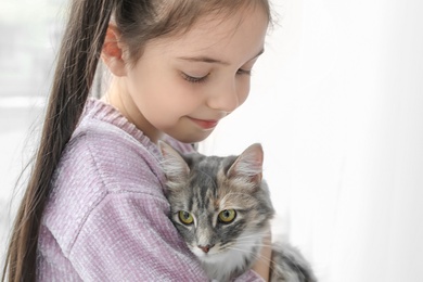 Photo of Cute little girl with cat near window at home