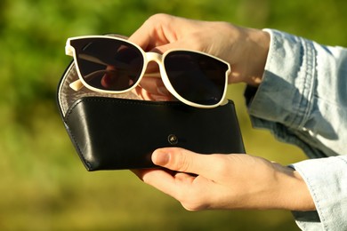 Photo of Woman holding sunglasses and case outdoors on sunny day, closeup