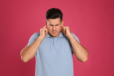 Photo of Emotional man covering ears with fingers on pink background