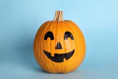 Photo of Pumpkin with drawn spooky face on light blue background. Halloween celebration