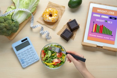 Photo of Woman eating tasty salad and calculating calories at wooden table, top view. Weight loss concept