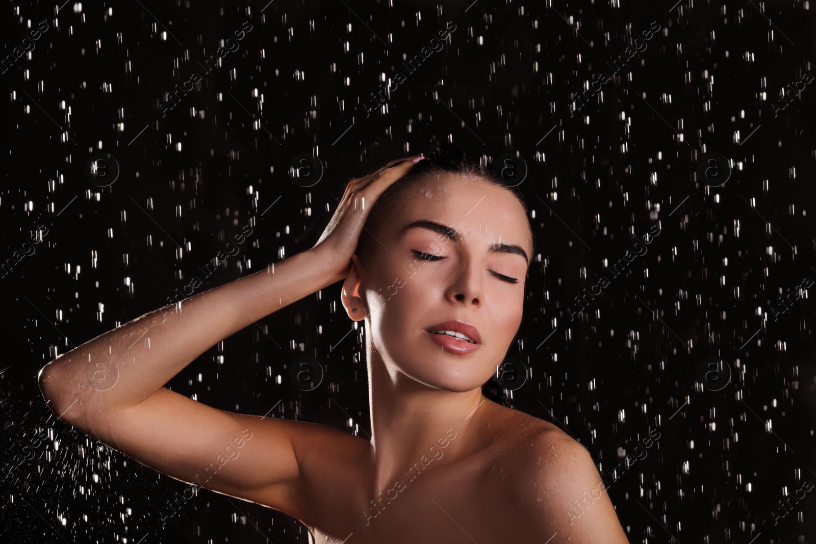 Photo of Young woman washing hair while taking shower on black background