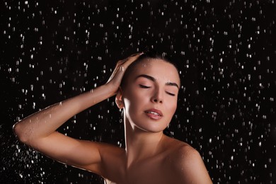 Young woman washing hair while taking shower on black background