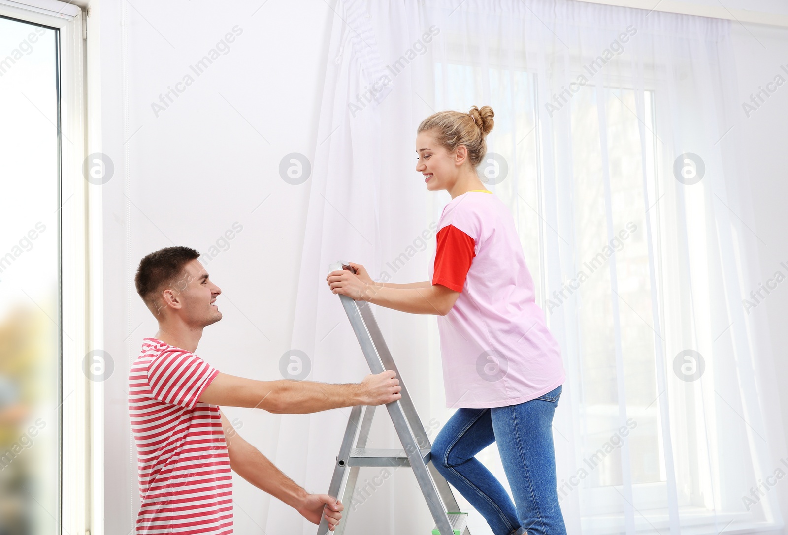 Photo of Young couple hanging window curtain indoors. Interior decor element