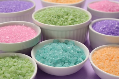Photo of Different types of aromatic sea salt on purple background, closeup