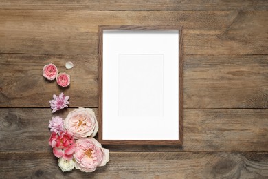 Photo of Empty photo frame and beautiful flowers on wooden table, flat lay. Space for design